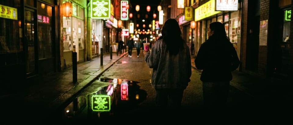 Two friends walking down a Chinatown street at night under hanging red lanterns and glowing neon signs