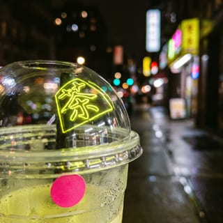Close-up of a condensation-covered boba cup with a glowing neon Chinese character 茶 on the dome lid